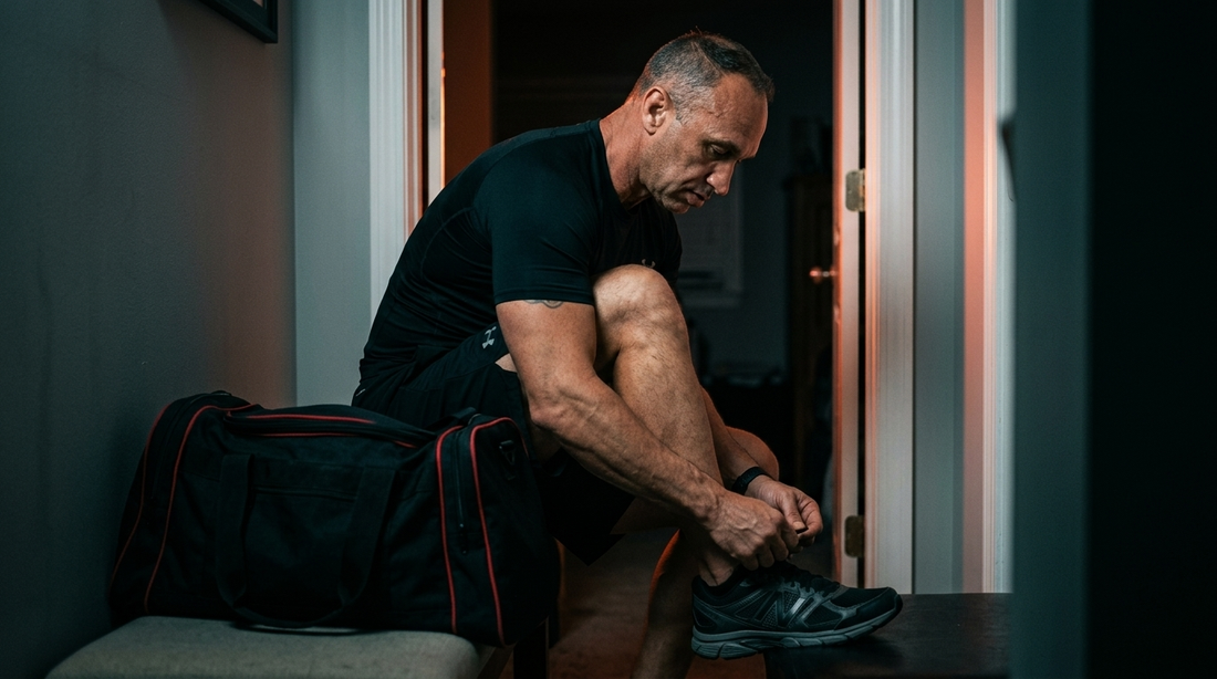 A middle aged man sitting quietly at a wooden table, hands resting and slightly clenched, morning light through a window